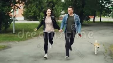 微笑的年轻人夫妻带着可爱的狗在公园里奔跑，享受活动，手牵着手